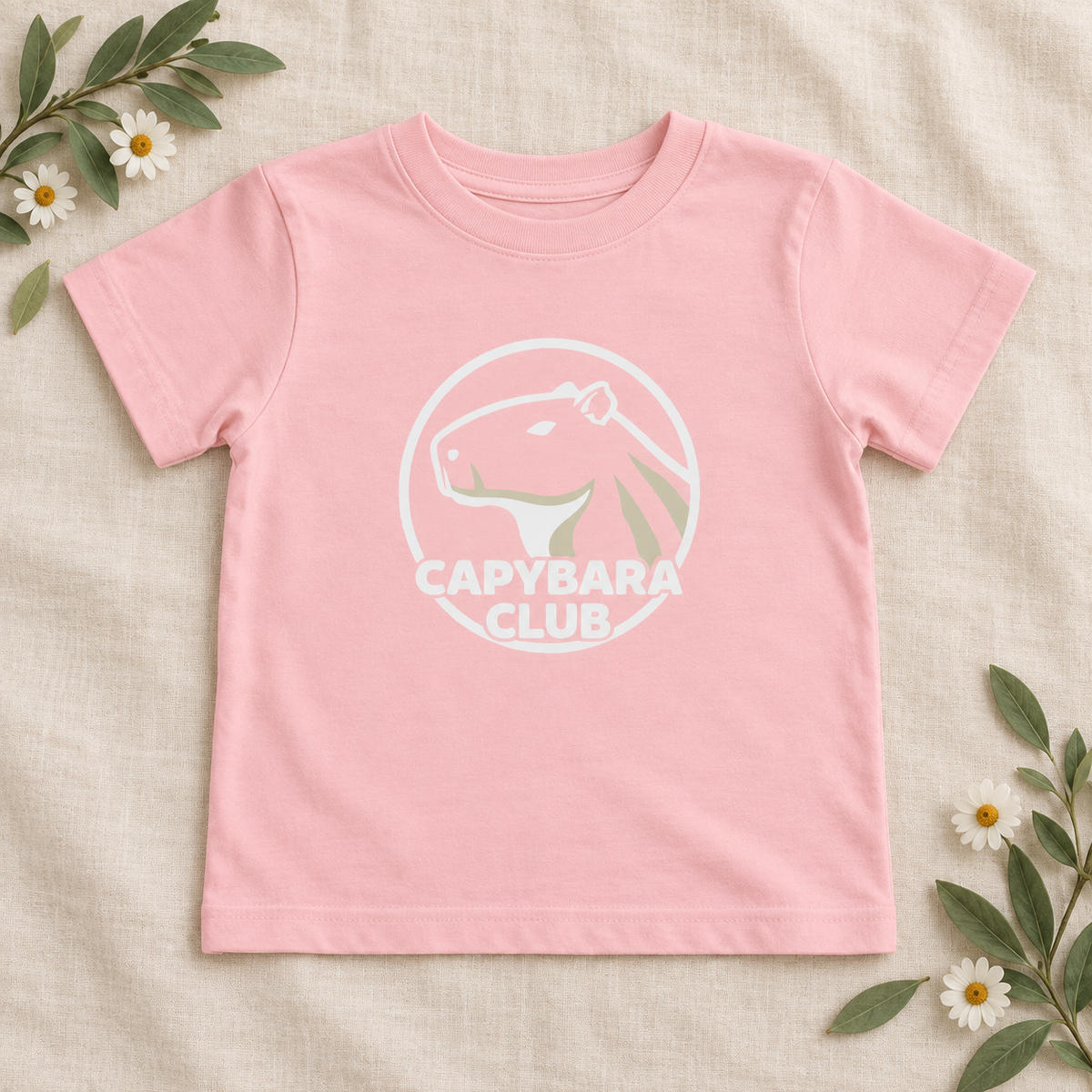 AI-created flat lay: Pink Capybara Club toddler tee with white artwork and botanical styling.