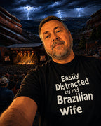 Man wearing a black t-shirt with text in front of a concert venue with lightning in the background