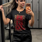 Woman taking a mirror selfie wearing a black t-shirt with a red and gold design.