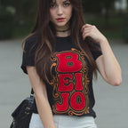 Woman wearing a black t-shirt with red and orange text, standing outdoors.