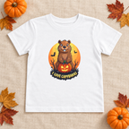 AI-created flat lay: White I Love Capybaras Halloween toddler tee on linen with pumpkins and fall leaves.