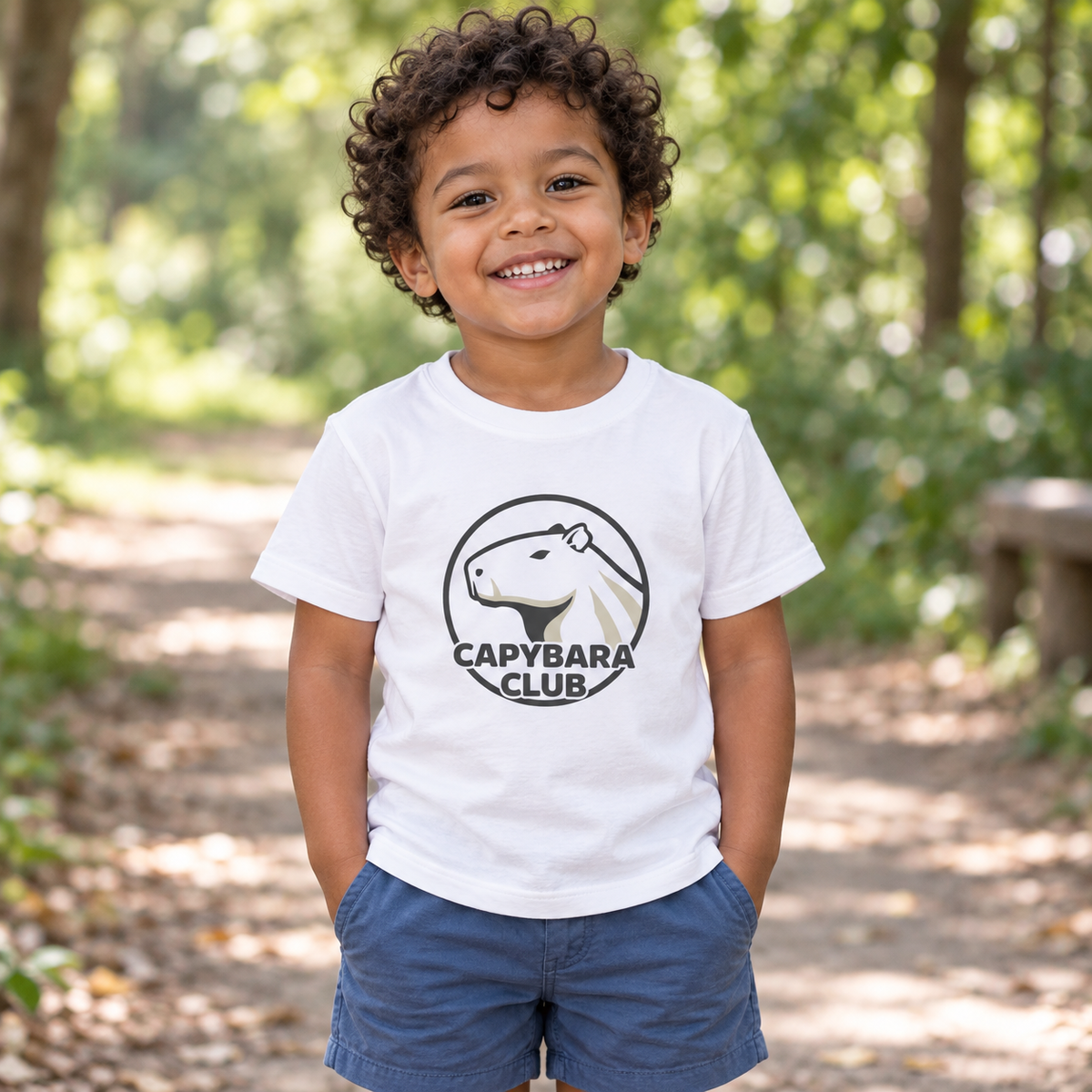 AI-created lifestyle mockup: White Capybara Club toddler tee on a child in a leafy park.